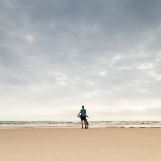 Woman standing on sandy beach with bike