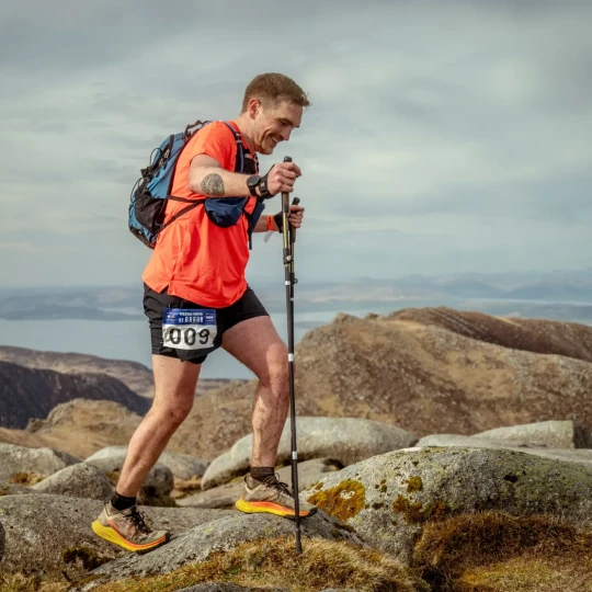 Man using trekking poles and climbing over rocks