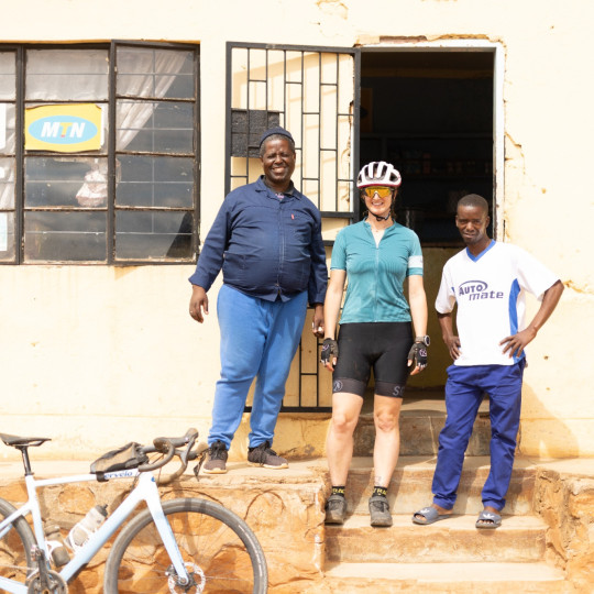 Three people stood outside of a building in the sunshine and smiling