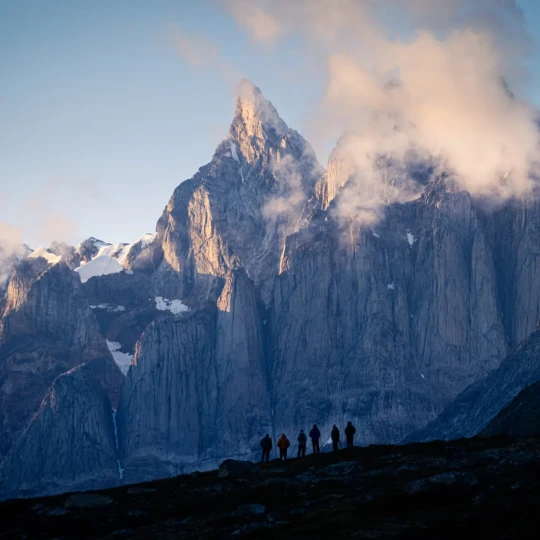 Six participants stood on rocky terrain, looking up at snow-topped mountains