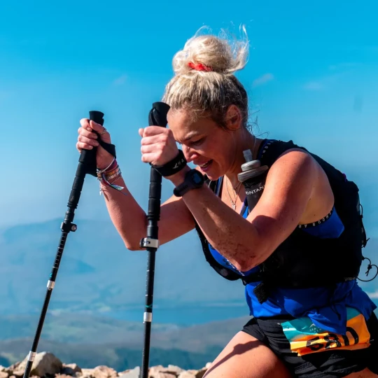 Woman using trekking poles and walking up mountain