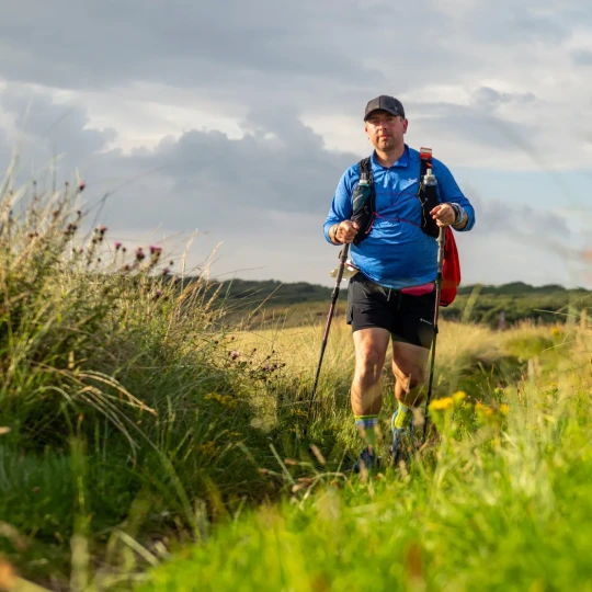 Man walking along trail with grass either side