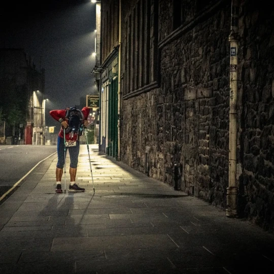 Participant leaning over trekking poles in urban setting at night