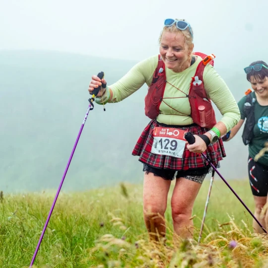 Two women walking on grass and using trekking poles