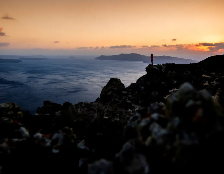 Person stood on rocky ledge, looking out at sunset