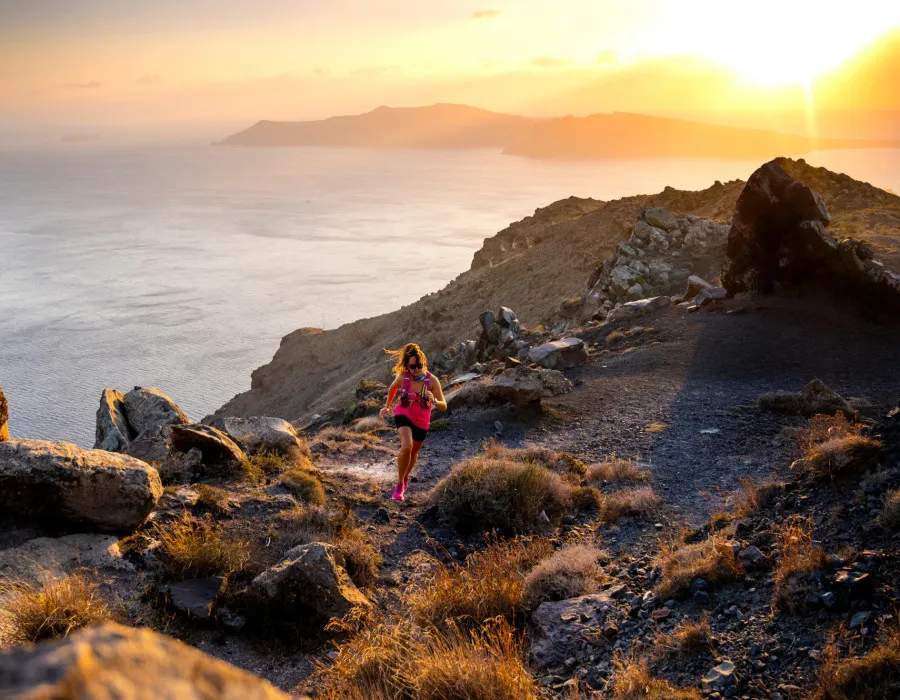 Woman running up rocky terrain with sunset behind her