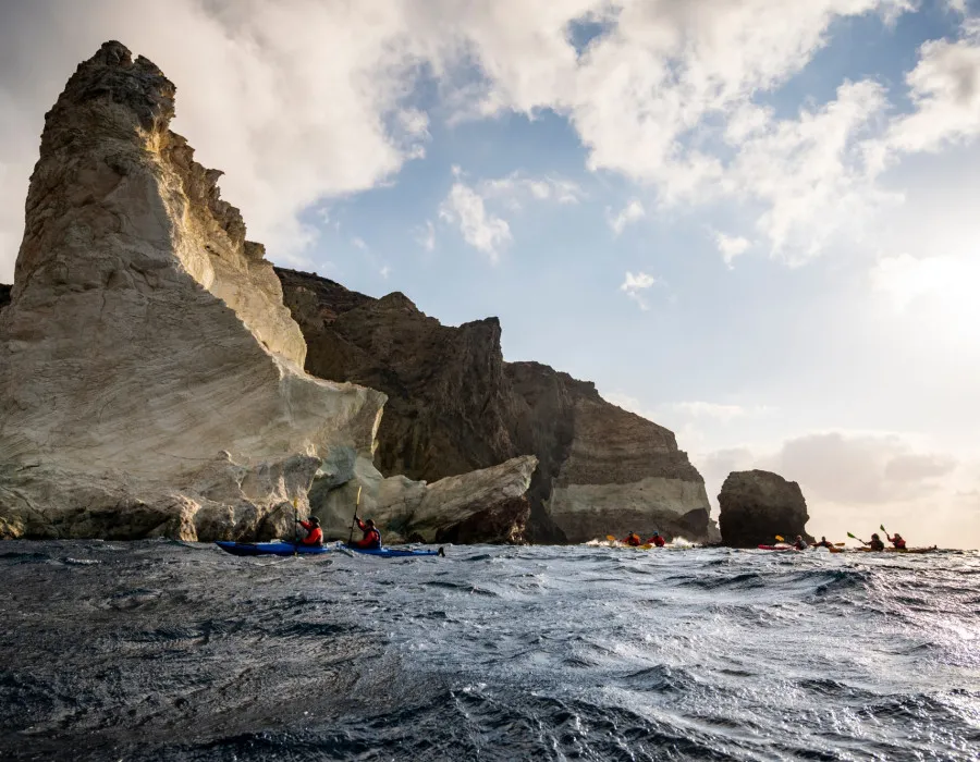 Participants kayaking through sea with cliffs behind them