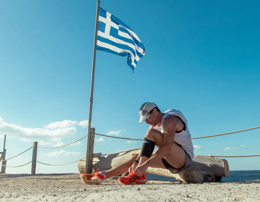 Man sat, tying shoe laces with Greek flag next to him