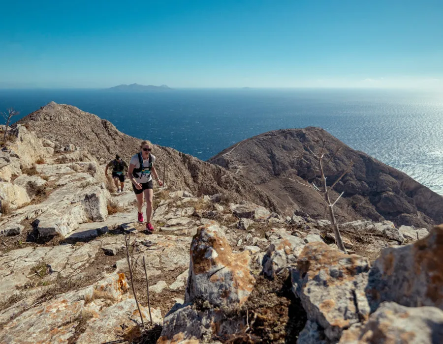 Man running up rocky terrain with sea behind them