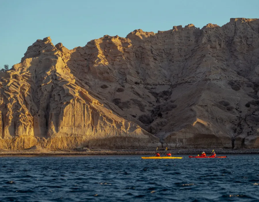 Participants kayaking past rocky cliffs