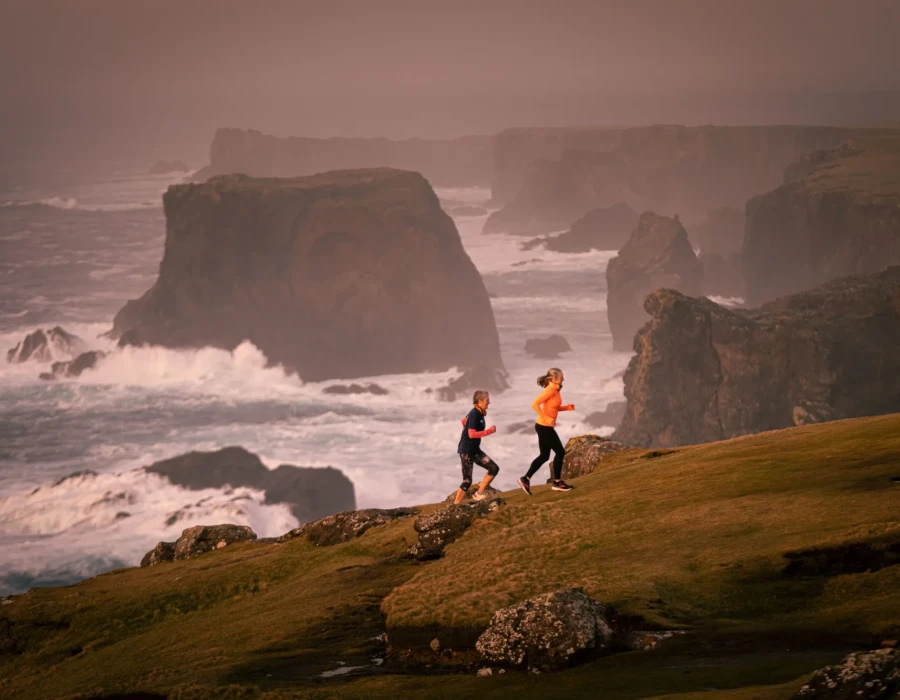 Women running up hill with cliffs and sea behind them
