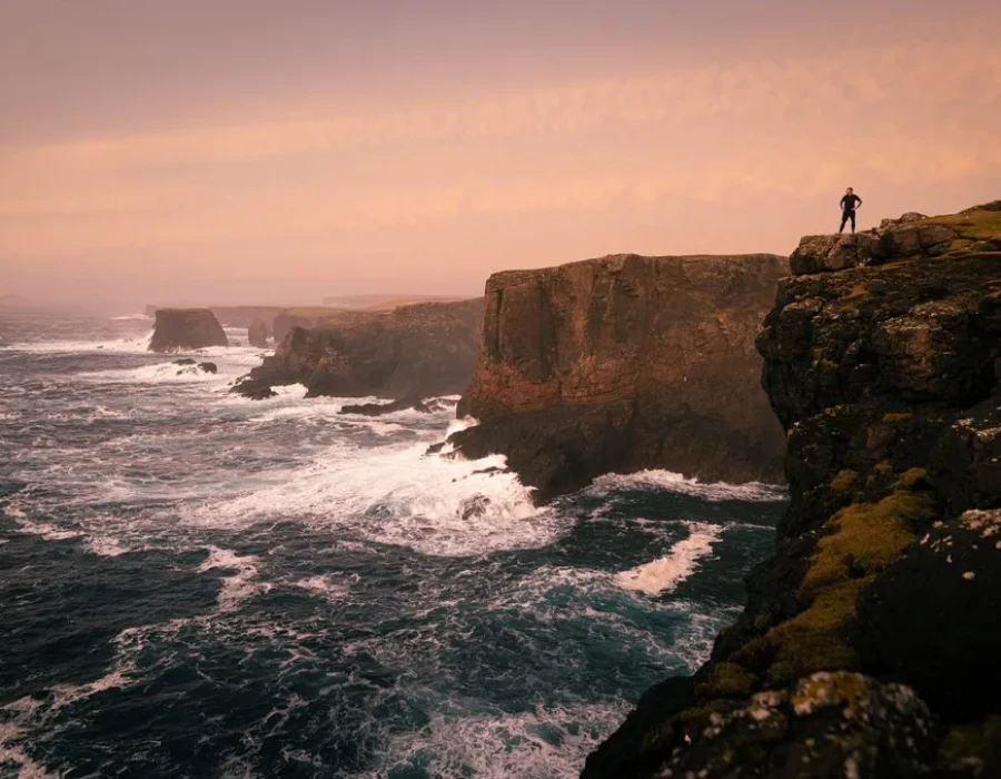 Person stood on cliff with colourful sky above them