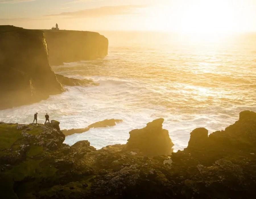 People stood on cliff edge, looking out at sea and sun