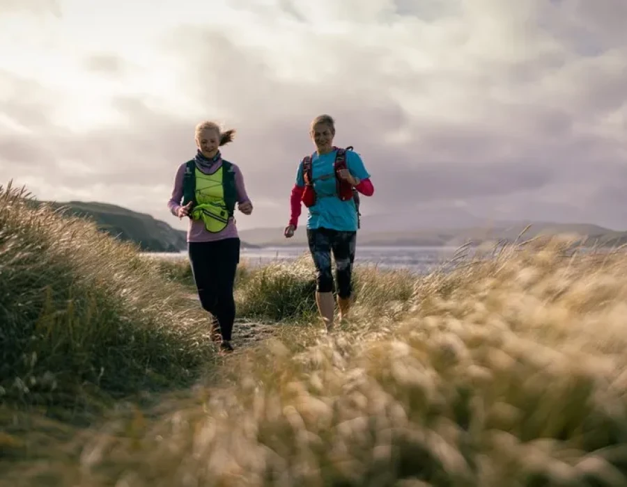 Women running along grassy coastline