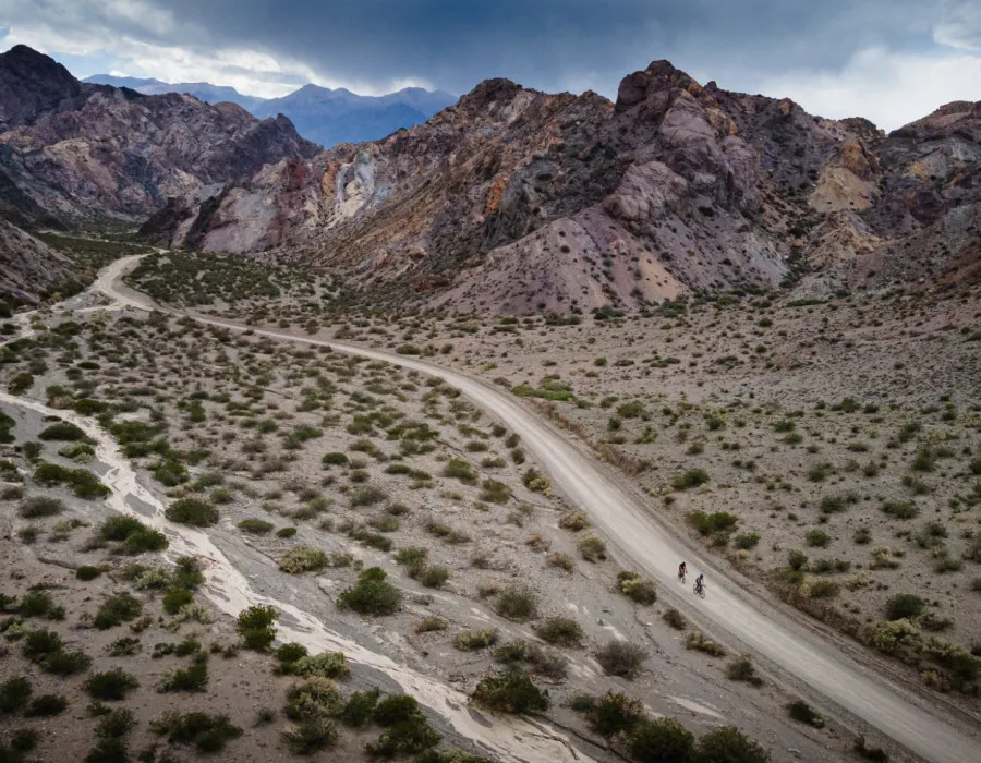 Cyclists riding along dusty path with mountains behind