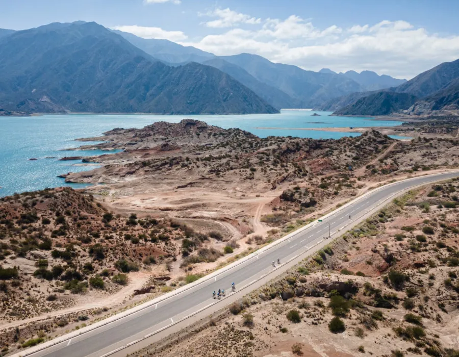 Cyclists riding along road with water and mountains behind