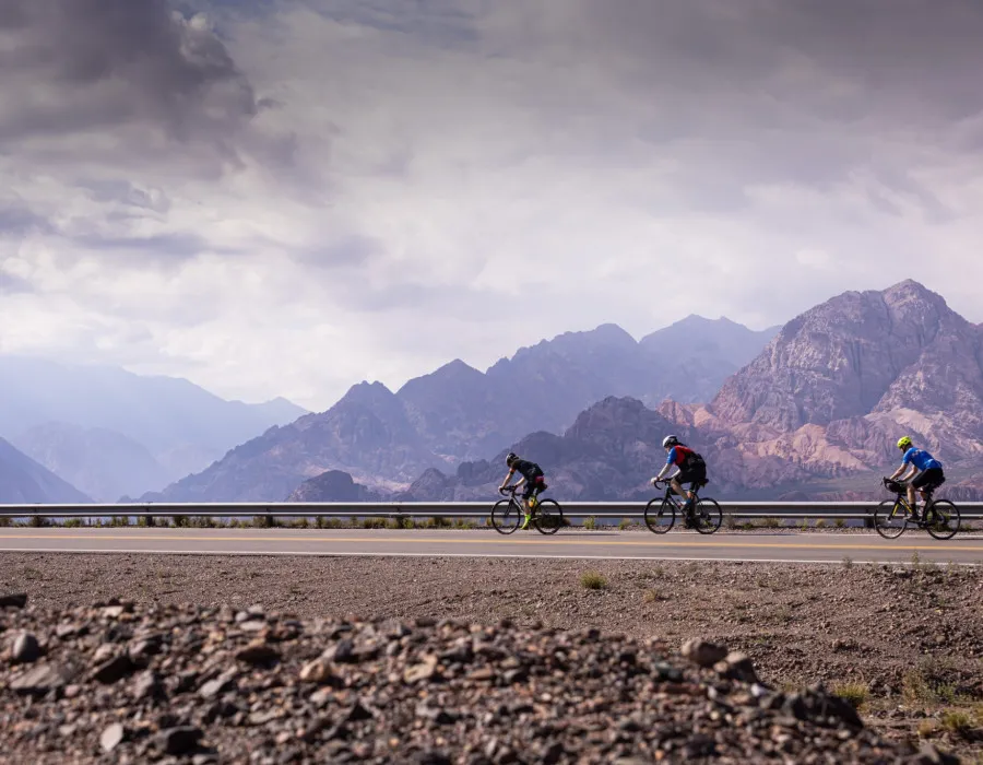 Cyclists riding along road with mountains in background