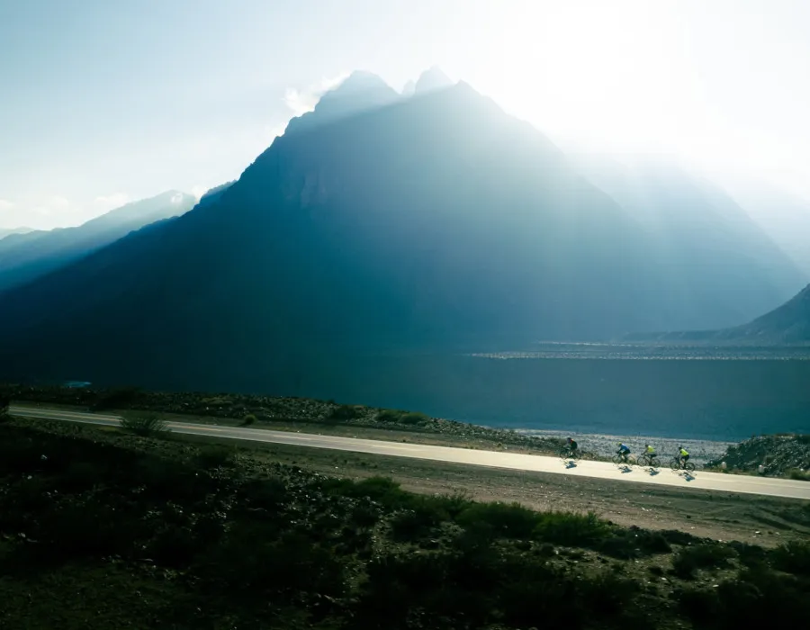 Cyclists riding along road past mountains