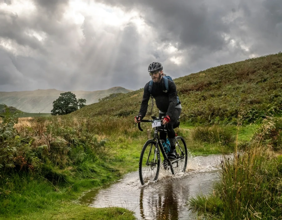 Man cycling through water with greenery either side of him