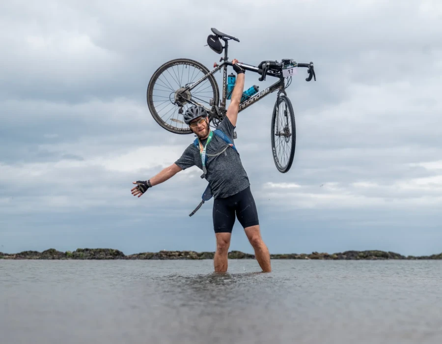 Man stood in water and holding his bike above his head