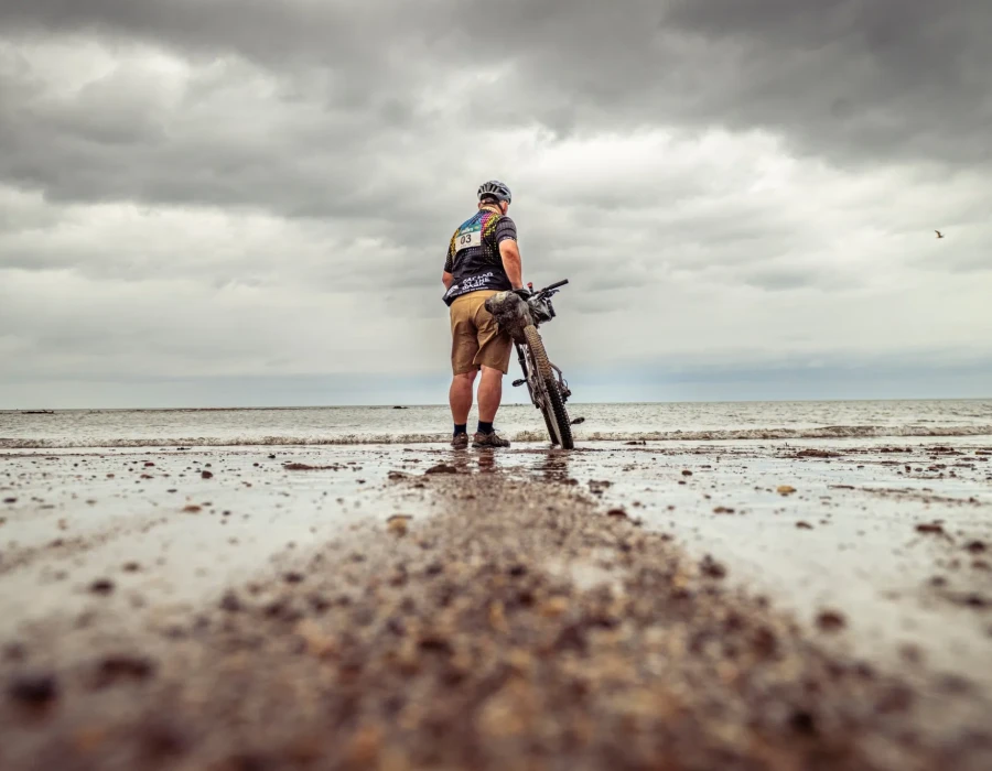 Man walking on wet sand with bike