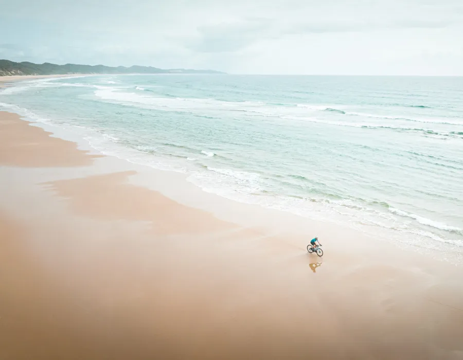 Woman cycling along sandy coastline