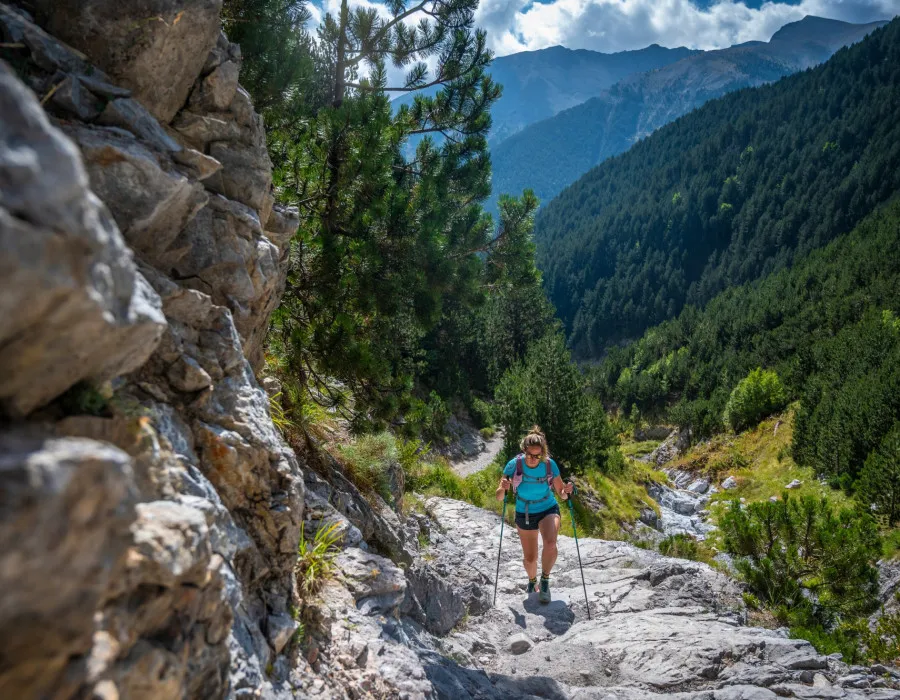 Woman hiking up rocky terrain with forests behind her