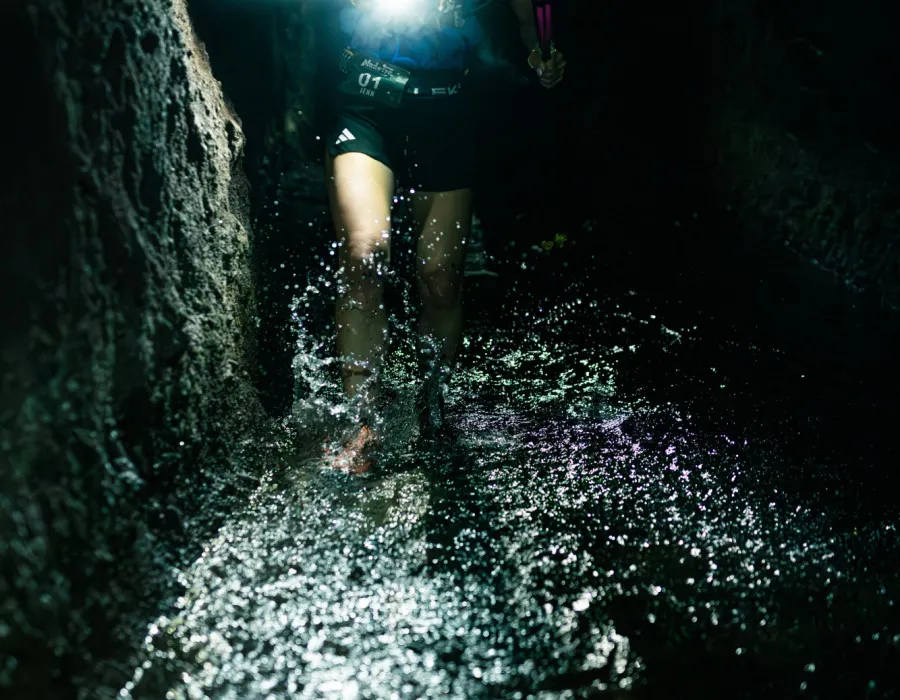 Participant holding a torch and walking through dark tunnel with shallow water
