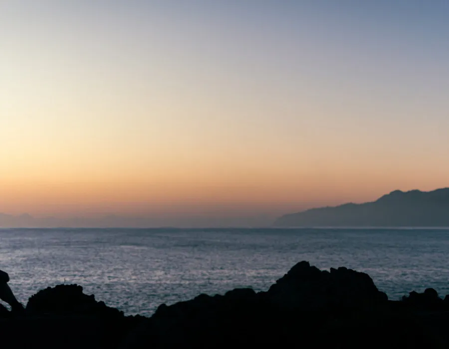 Participant sat on rocks, looking out to sunset over sea