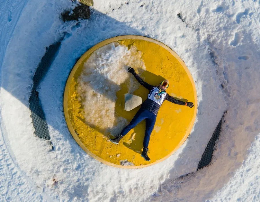 Rat Race Participant lying with their arms out and face up on a bright yellow circle, surrounded by snow