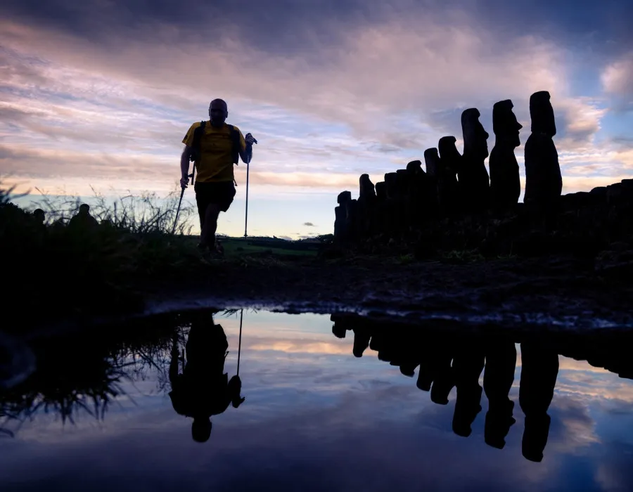 Silhouette of a man running through water, with statues to his left and a colourful sky behind