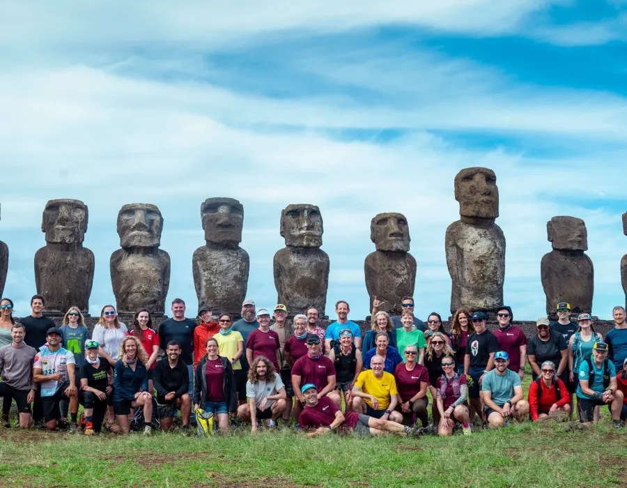 Group of smiling participants in colourful clothes with statues behind them and a blue sky above
