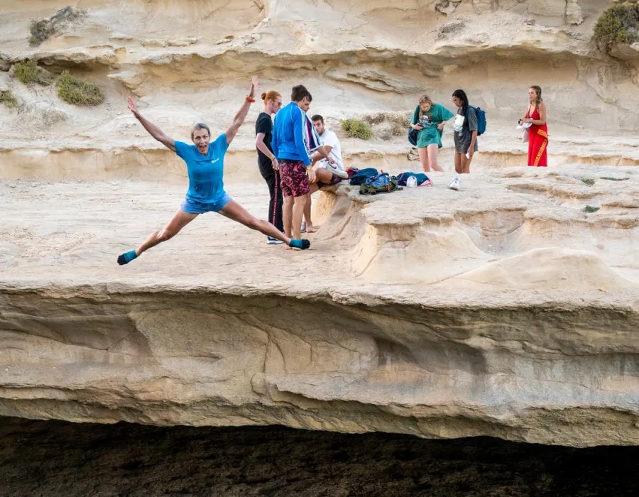 Group of participants stand on rock as woman jumps into water
