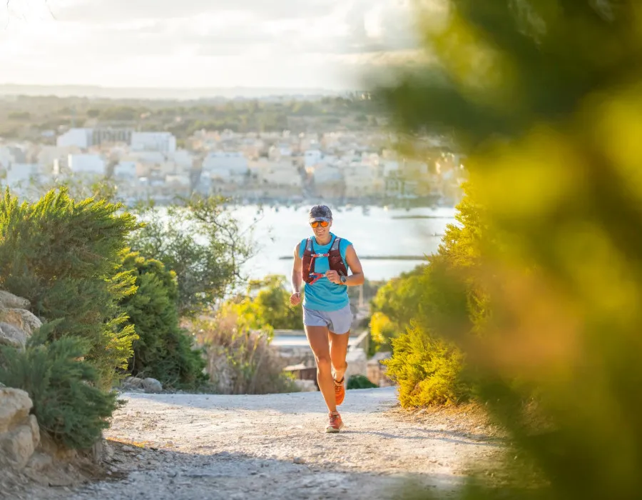 Woman running on a dusty path in the sunshine, surrounded by greenery