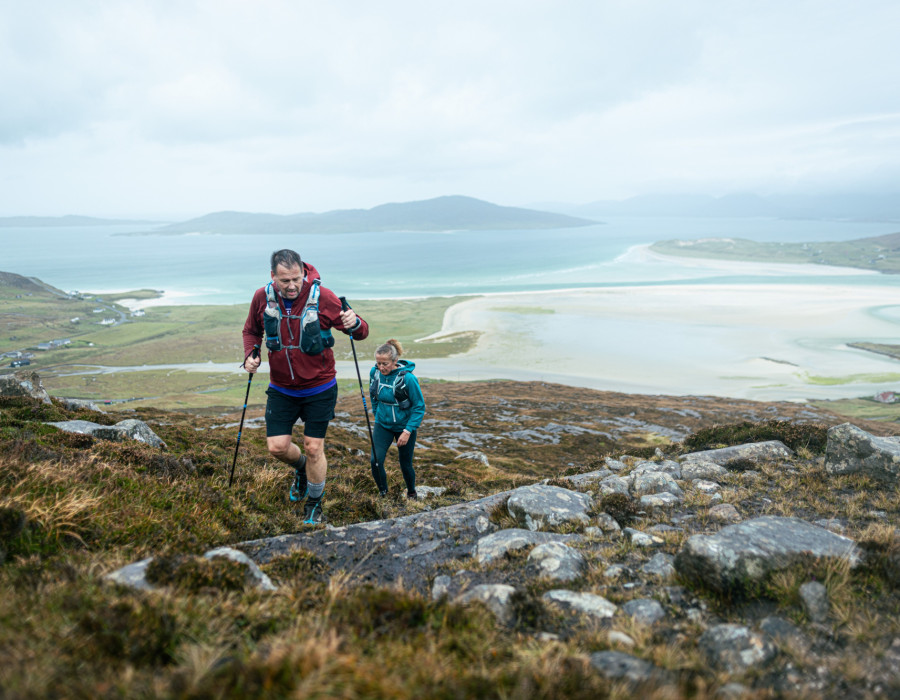 Man and woman walking over grass and rocky terrain