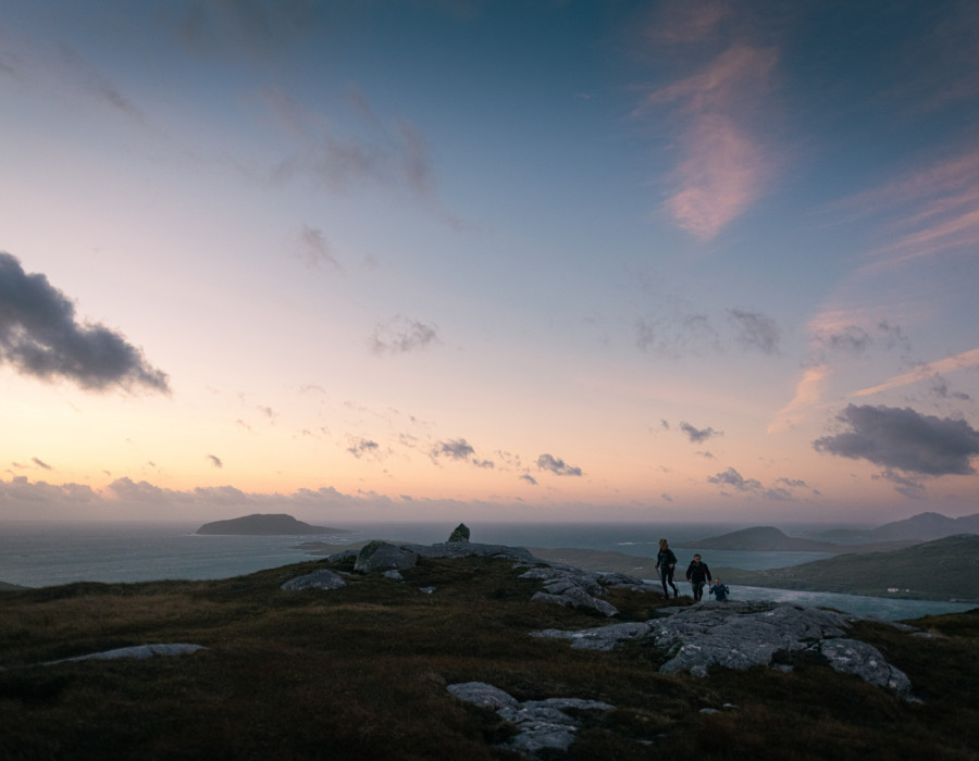 Participants running over grass and rocks with colourful sky above them
