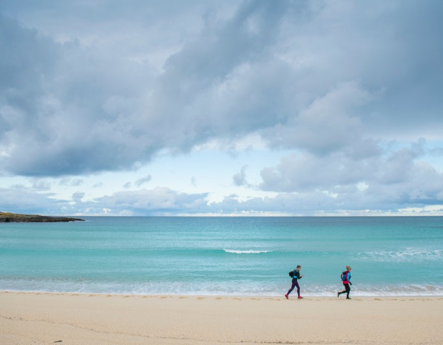 People running on sandy beach with clear sea behind