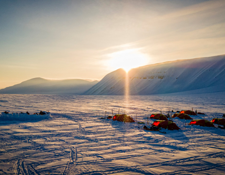 Tents pitched in deep snow with low sign behind a mountain
