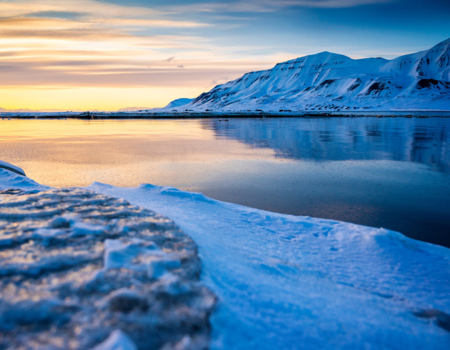 Icy water with a colourful sky above and snowy mountains