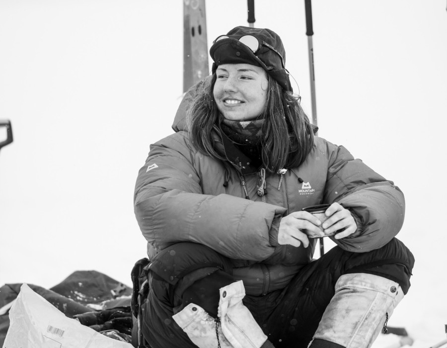 Woman sat on snow, holding a warm drink and smiling