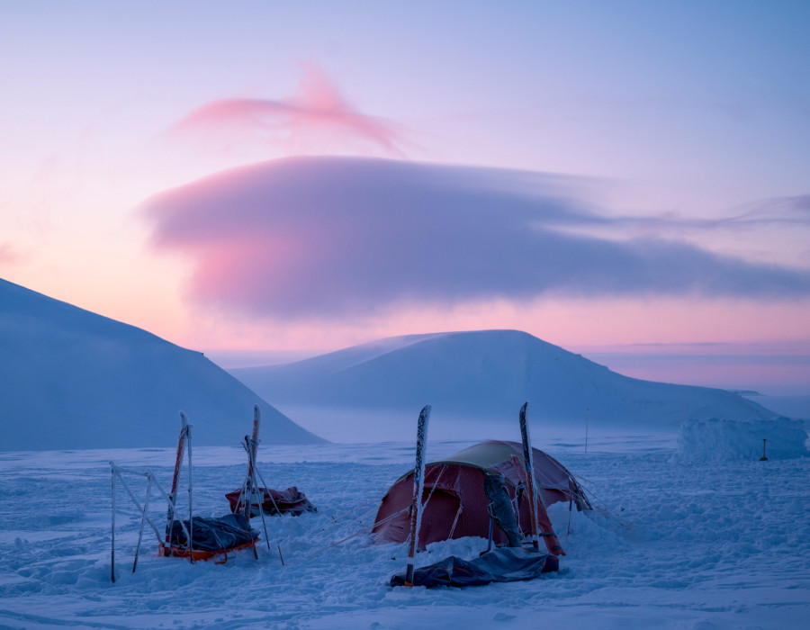Tent pitched in deep snow with a colourful sky behind