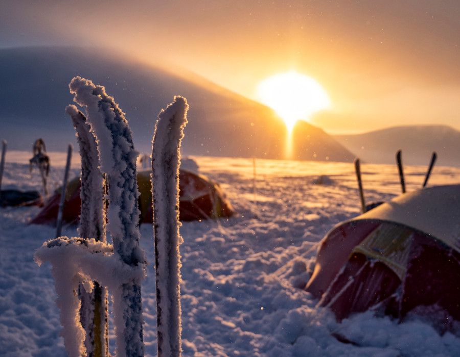 Snow-covered tents and a low, colourful sun behind
