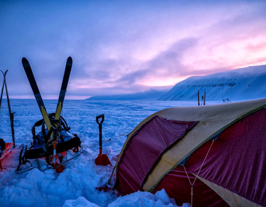 Tent pitched in deep snow with a colourful sky behind