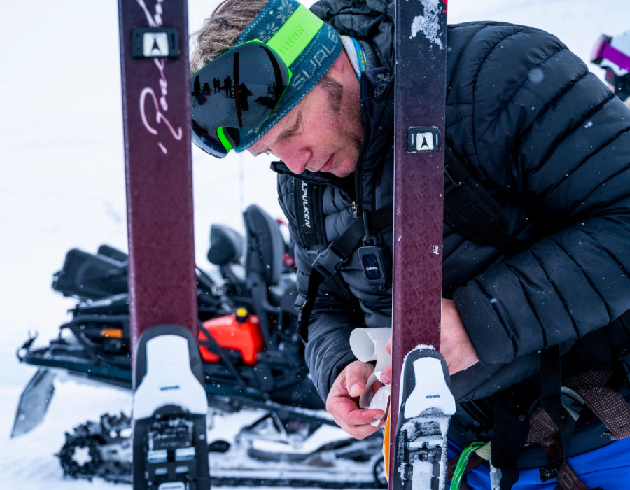 Man fixing skis in a snowy, white environment