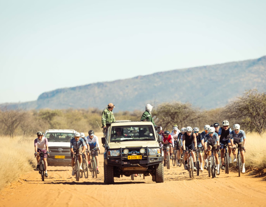 Cyclists and two vehicles moving along dusty road beneath sun