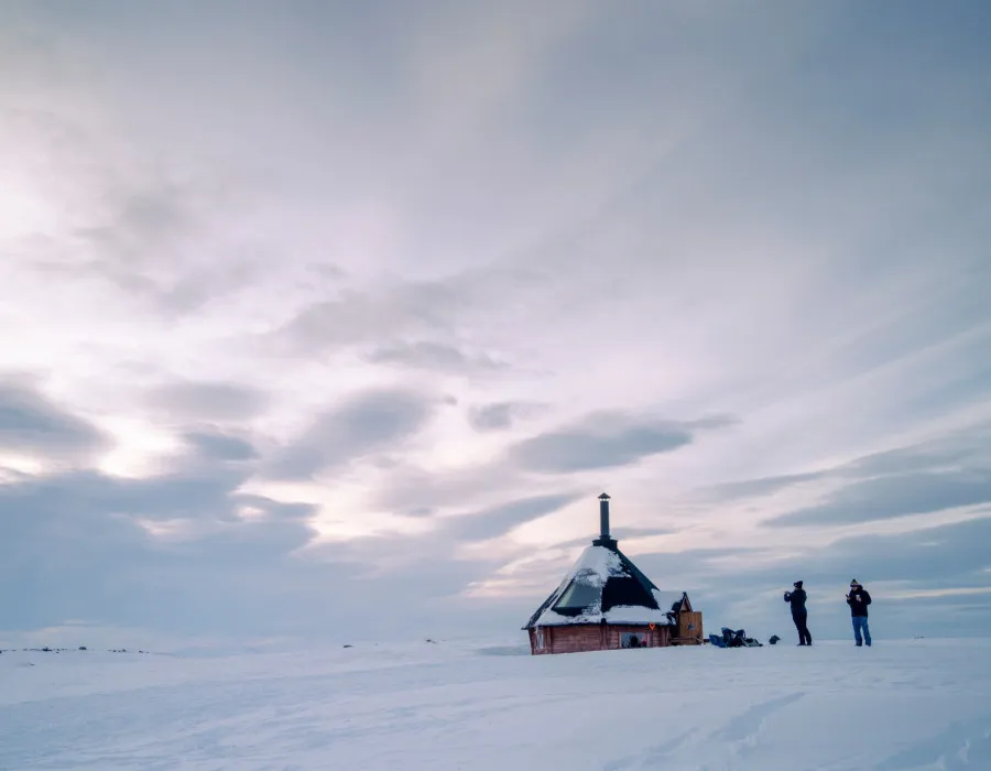 A snowy background and a couple of participants stood to the right of a yurt