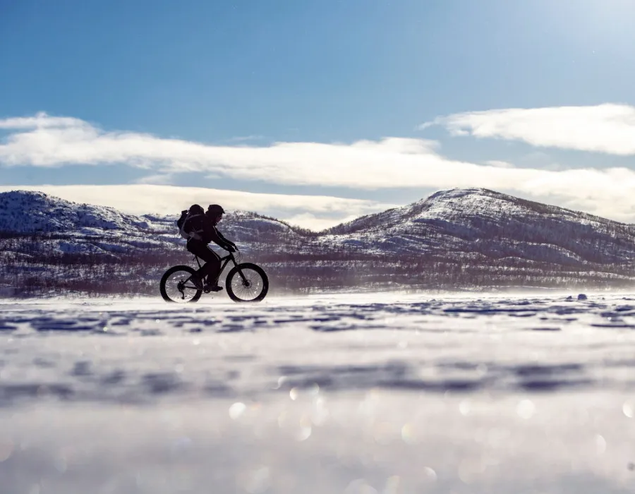 Single cyclist riding across a snowy landscape on a fat bike