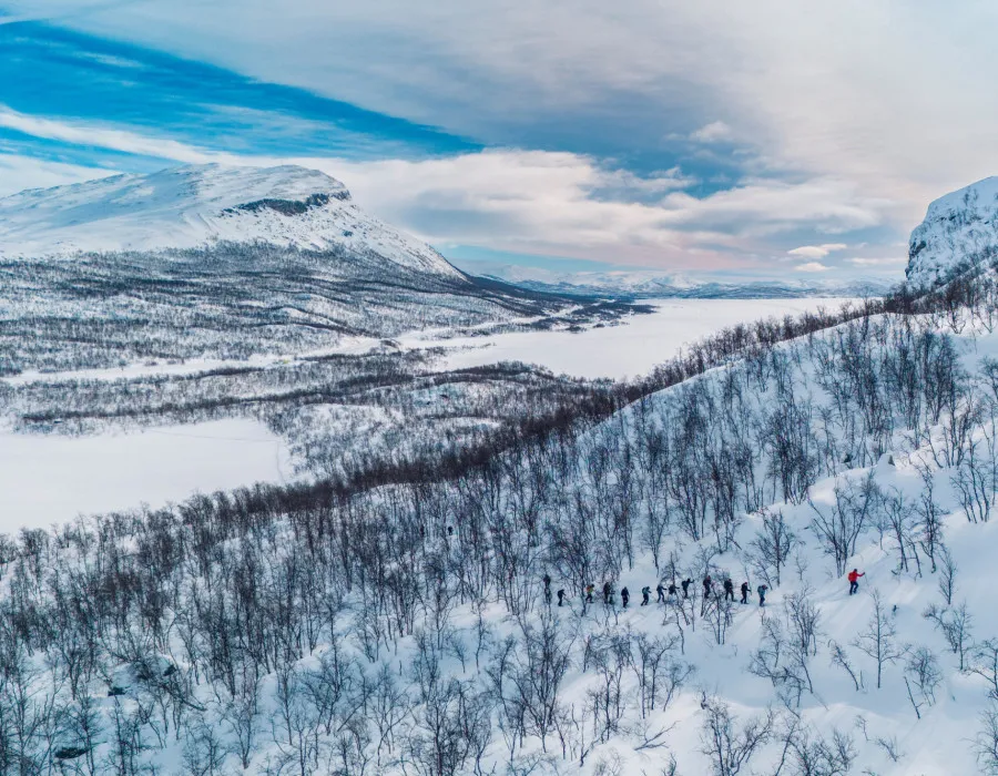 Group of participants making their way through a snowy forest with mountains in the background