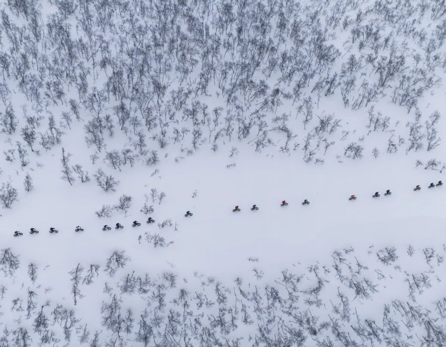 Aerial view of a group of cyclists riding fat bikes along a snow-covered trail through a winter forest