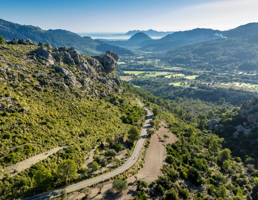 Rolling hills stretch across the countryside, with a winding road weaving through the landscape beneath a clear blue sky